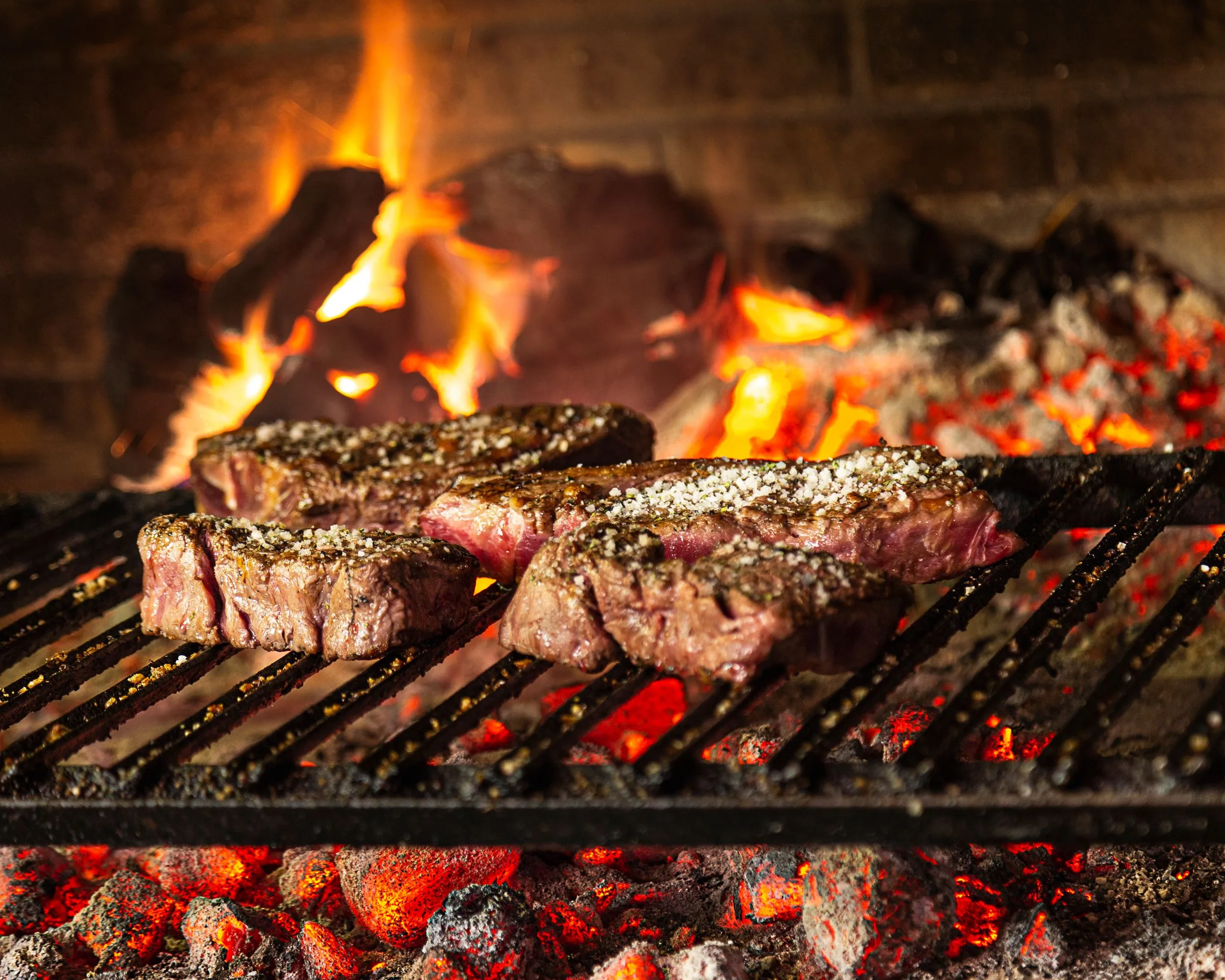 Cuatro txuletas sobre la parrilla de brasa de Asador Artebe, con las llamas al fondo