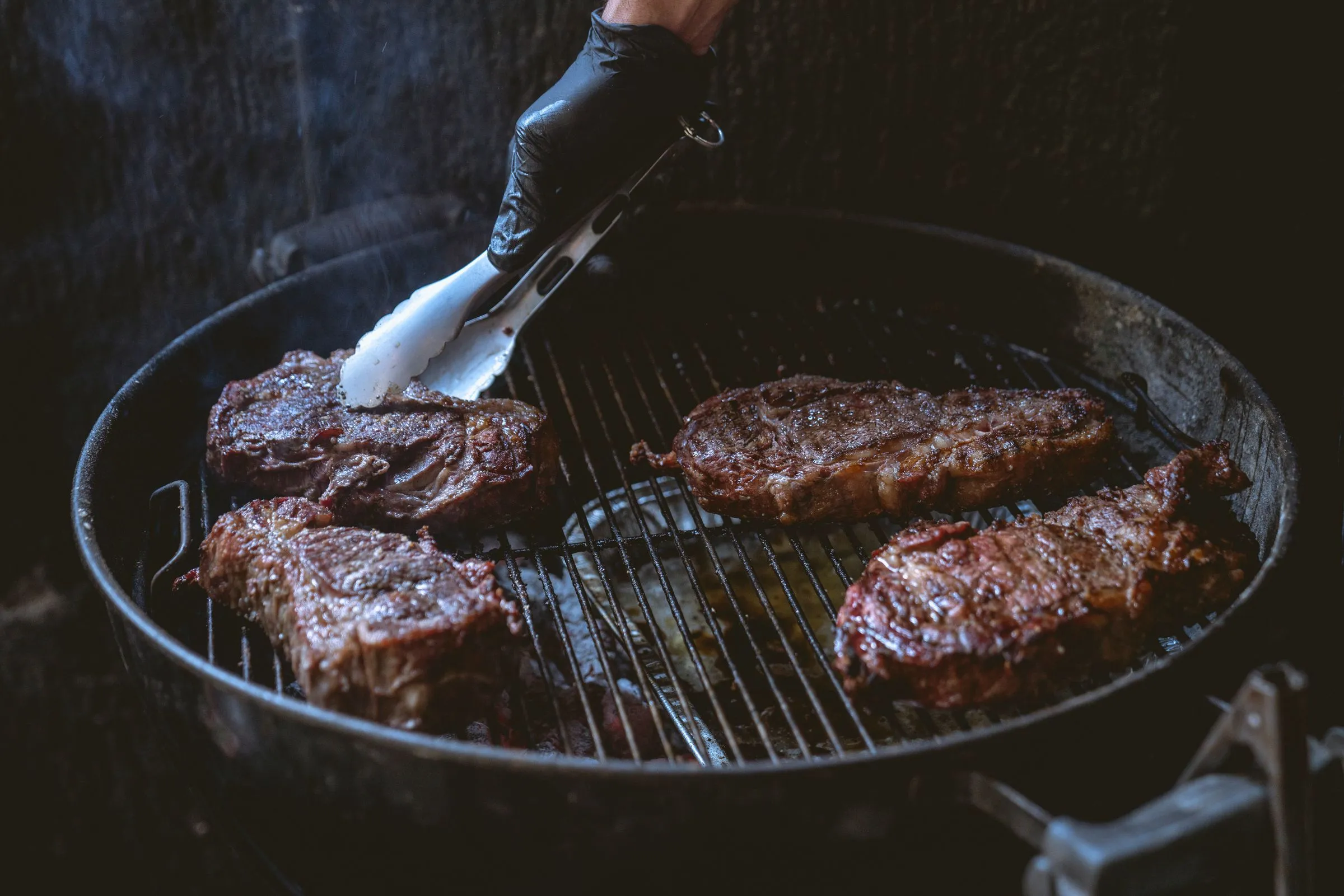 Parrillero girando piezas de carne con pinzas sobre una parrilla redonda de brasa