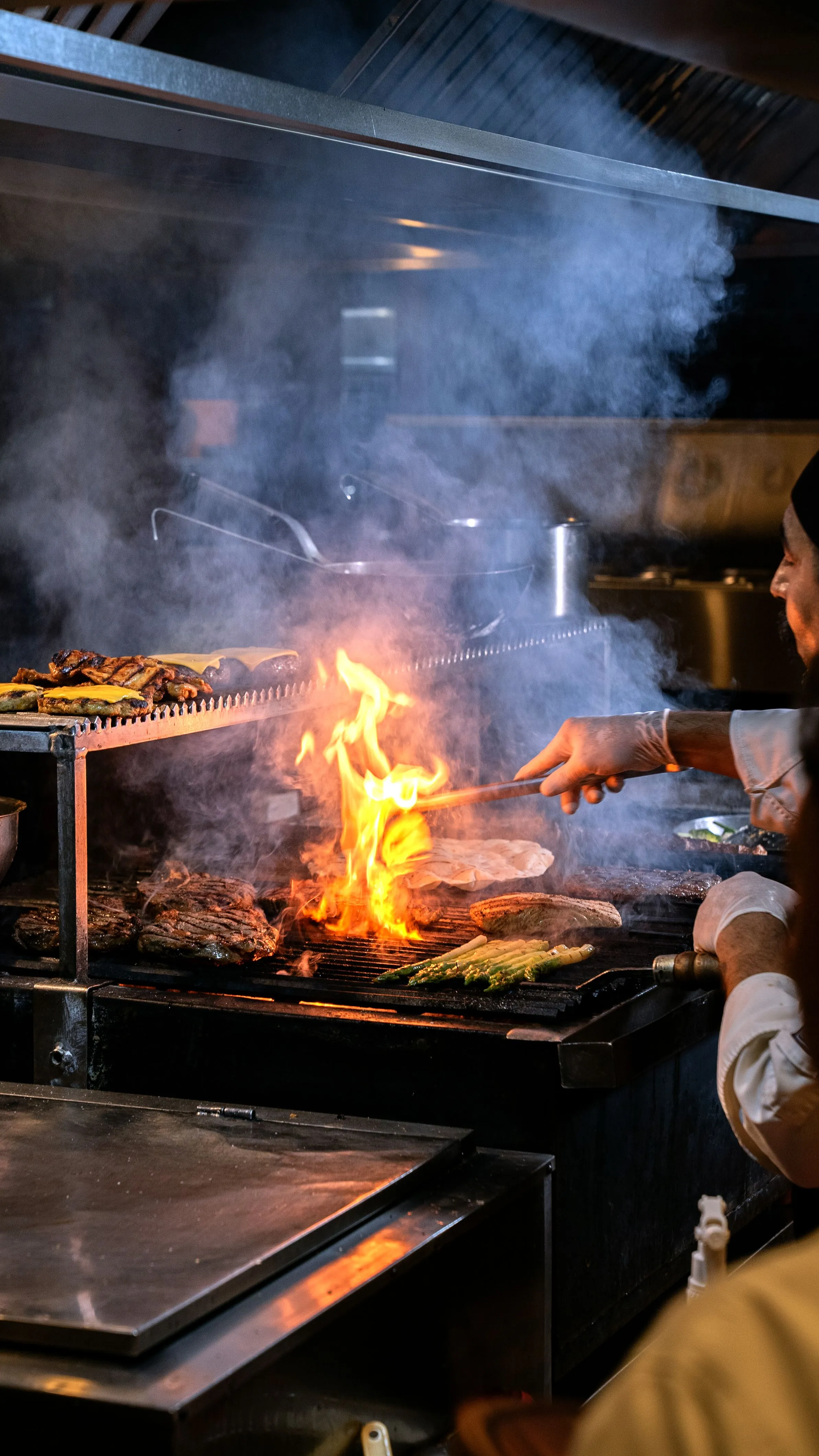 Interior de la cocina de Artebe con una llamarada y humo sobre la parrilla