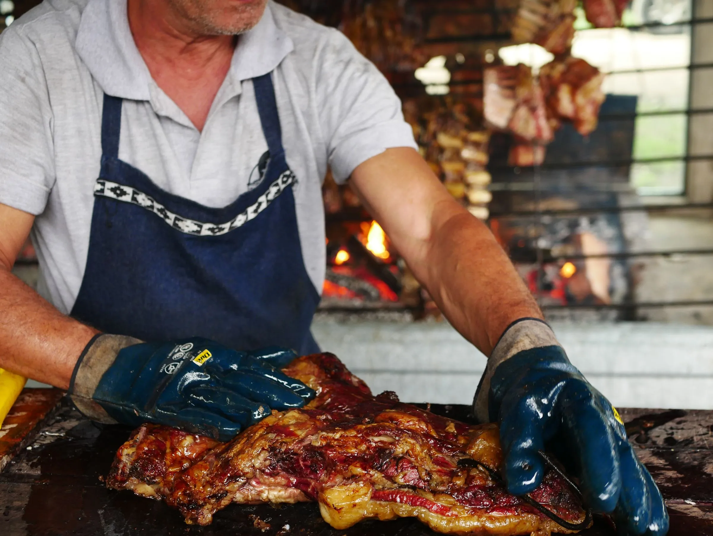Parrillero de Artebe con guantes de trabajo colocando una pieza grande sobre las brasas